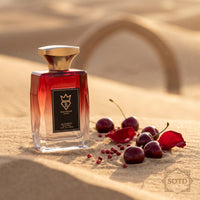 Bujairami Red Static Eau de Parfum 100ml bottle on desert sand with cherries, rose petals and pink peppercorns