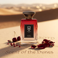 Bujairami Red Static Eau de Parfum 100ml bottle on a sand dune with cherries and scattered rose petals