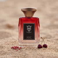 Bujairami Red Static Eau de Parfum 100ml bottle on fine sand with a pair of cherries